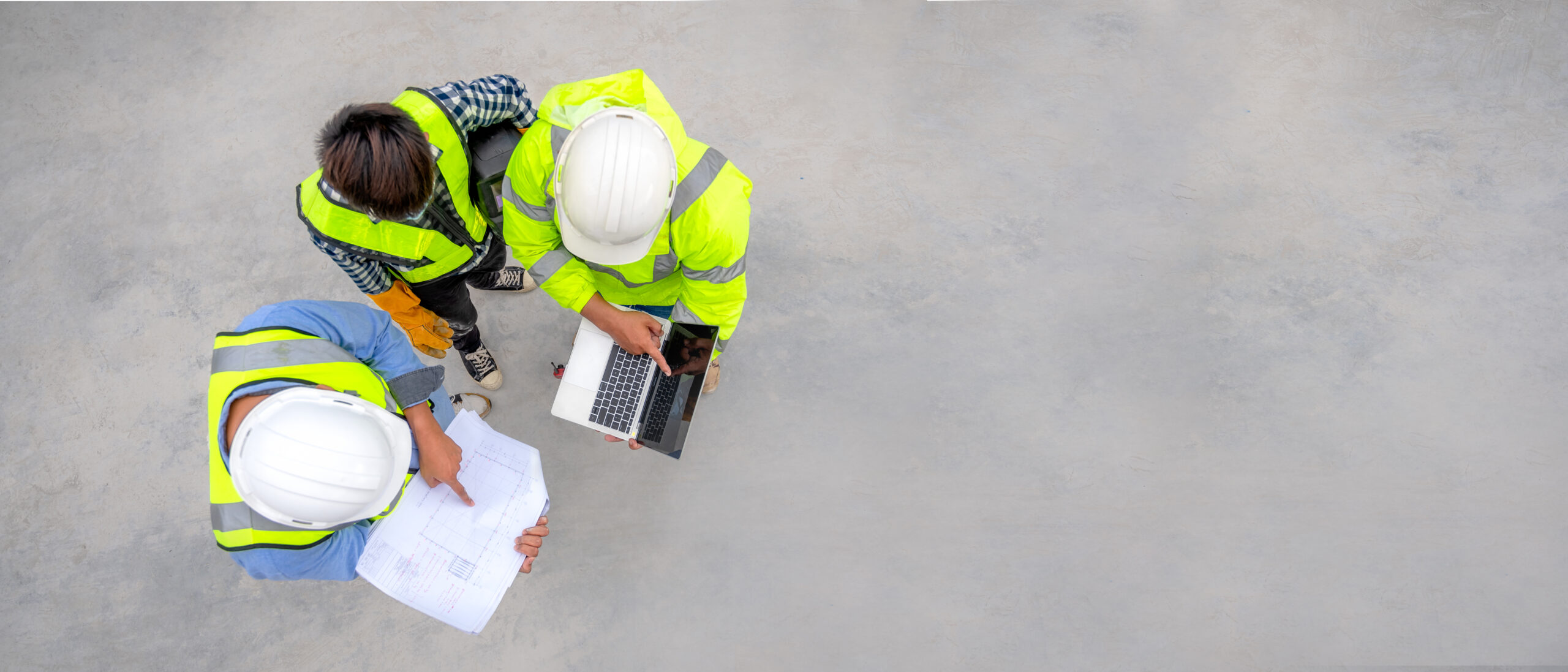 view from above of construction workers pouring over a computer and schematics